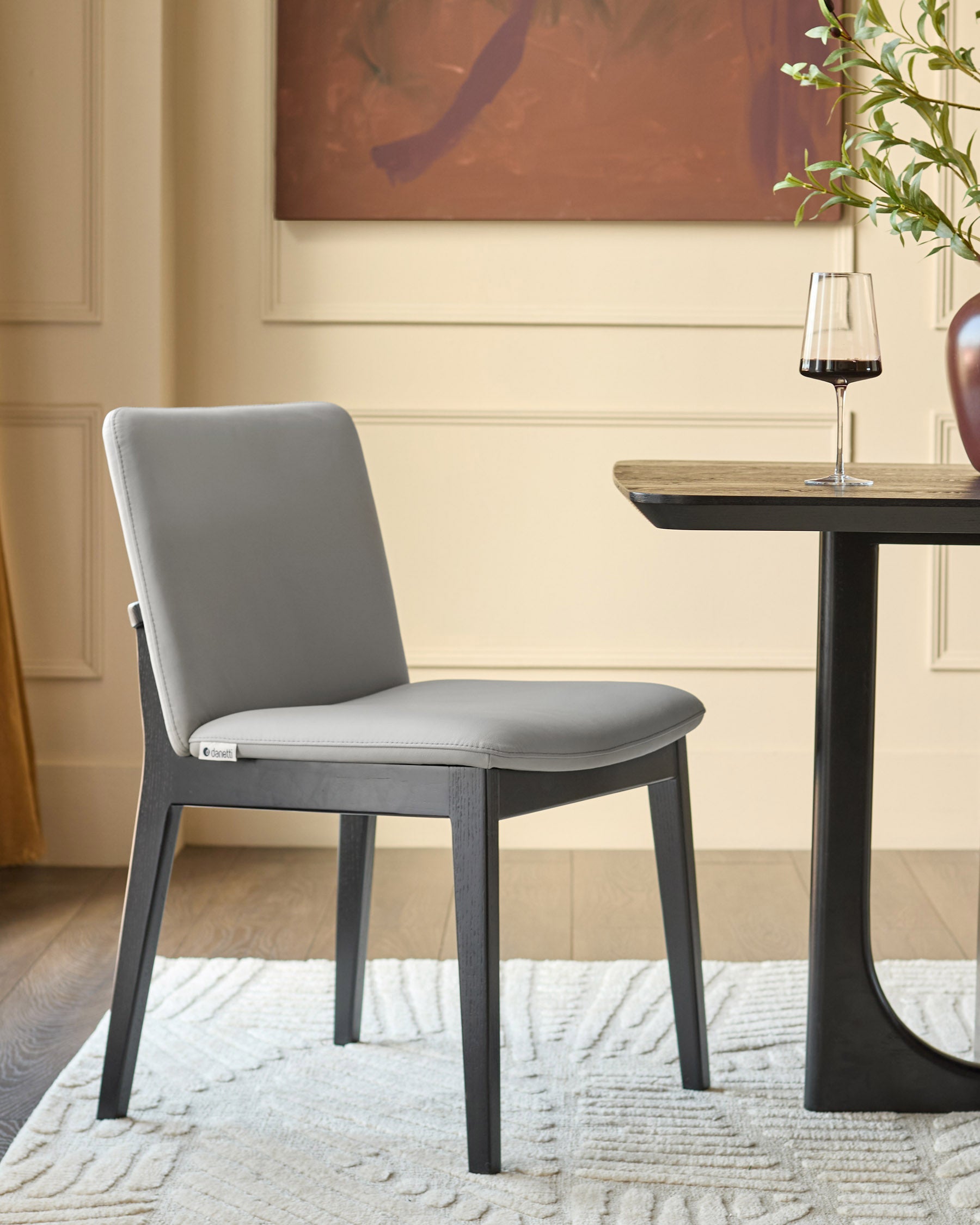 Otis dining chair in light grey leather with dark wood frame, shown in modern room setting next to side table.