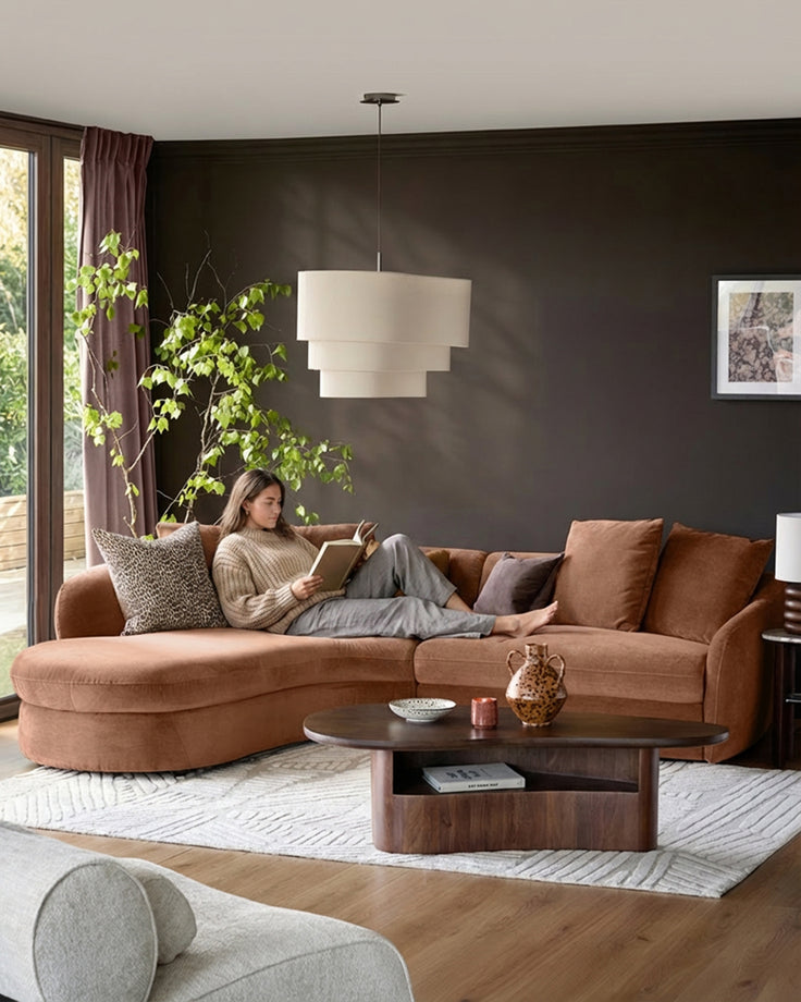 Apricot fabric left-hand corner chaise sofa with curved arms, styled in a modern living room with dark walls.