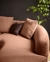 Apricot fabric corner chaise sofa with curved armrest, styled with brown and matching pillows against dark wall with trailing ivy.