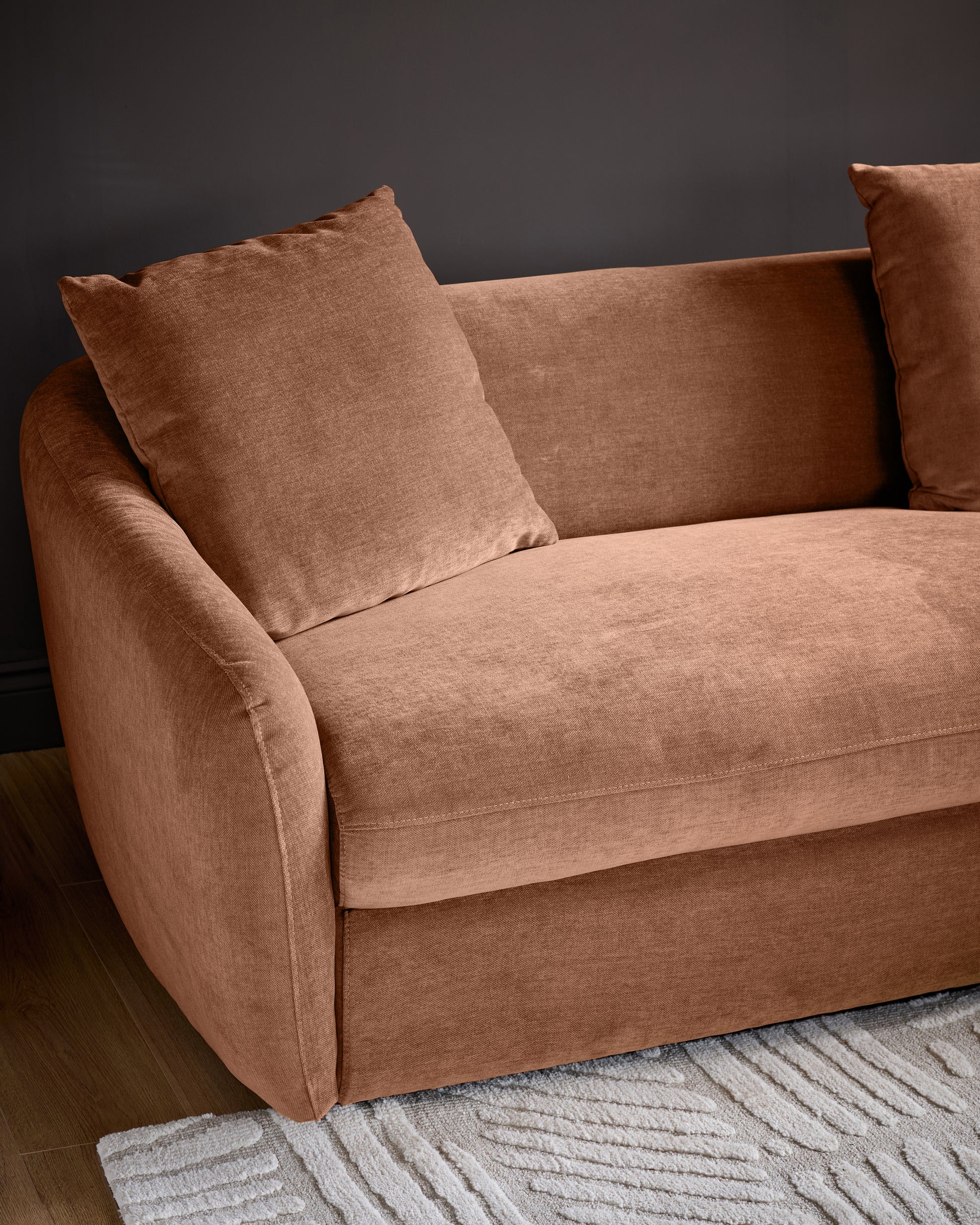 Apricot fabric right-hand corner chaise sofa with curved armrests and matching cushions, angled view against gray wall.