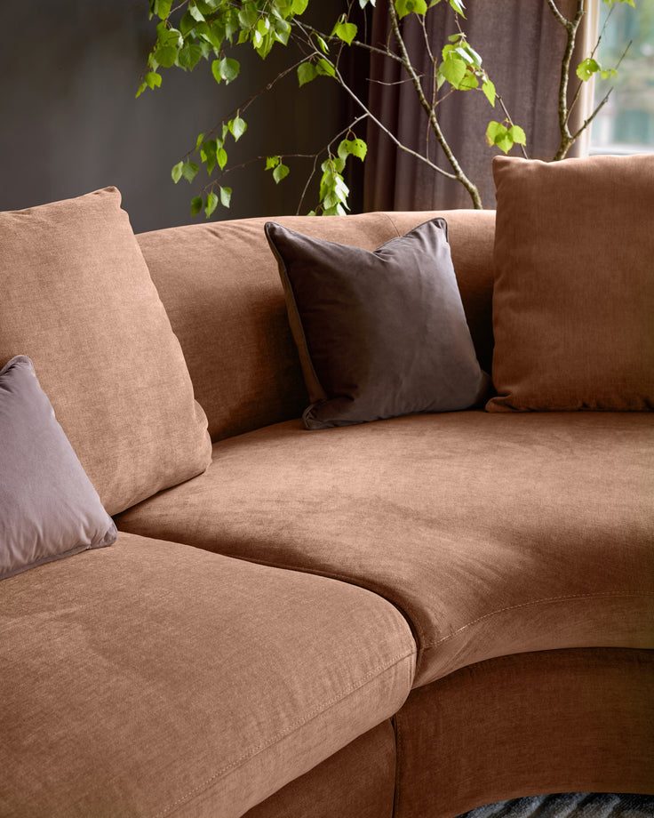 Ottilie right-hand corner chaise sofa in apricot fabric with dark brown scatter cushions, angled view.