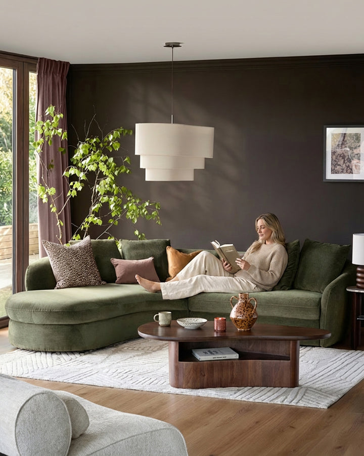 Olive-green left-hand corner chaise sofa in a modern living room setting, styled with colorful cushions and paired with a wooden coffee table.
