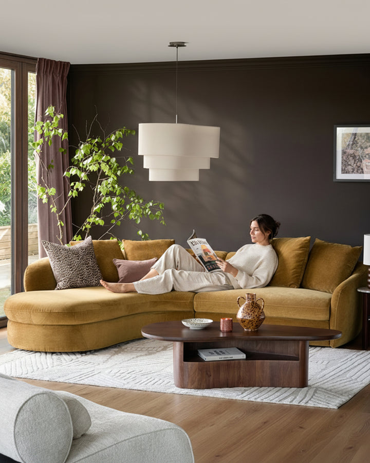 Ochre left-hand corner chaise sofa in a modern living room setting, paired with dark walls and wooden coffee table.
