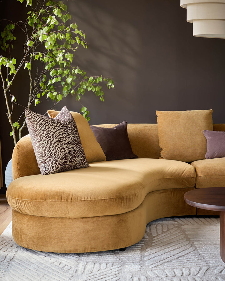 Ochre left-hand corner chaise sofa with curved design, styled with patterned and solid cushions in a modern living room setting.