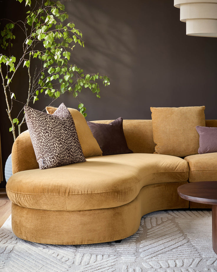 Ochre left-hand corner chaise sofa with curved design, styled with patterned and solid cushions in a modern living room setting.