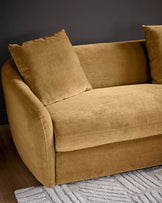 Ochre fabric right-hand corner chaise sofa with rounded arms and matching cushions, displayed against a dark background on a patterned rug.