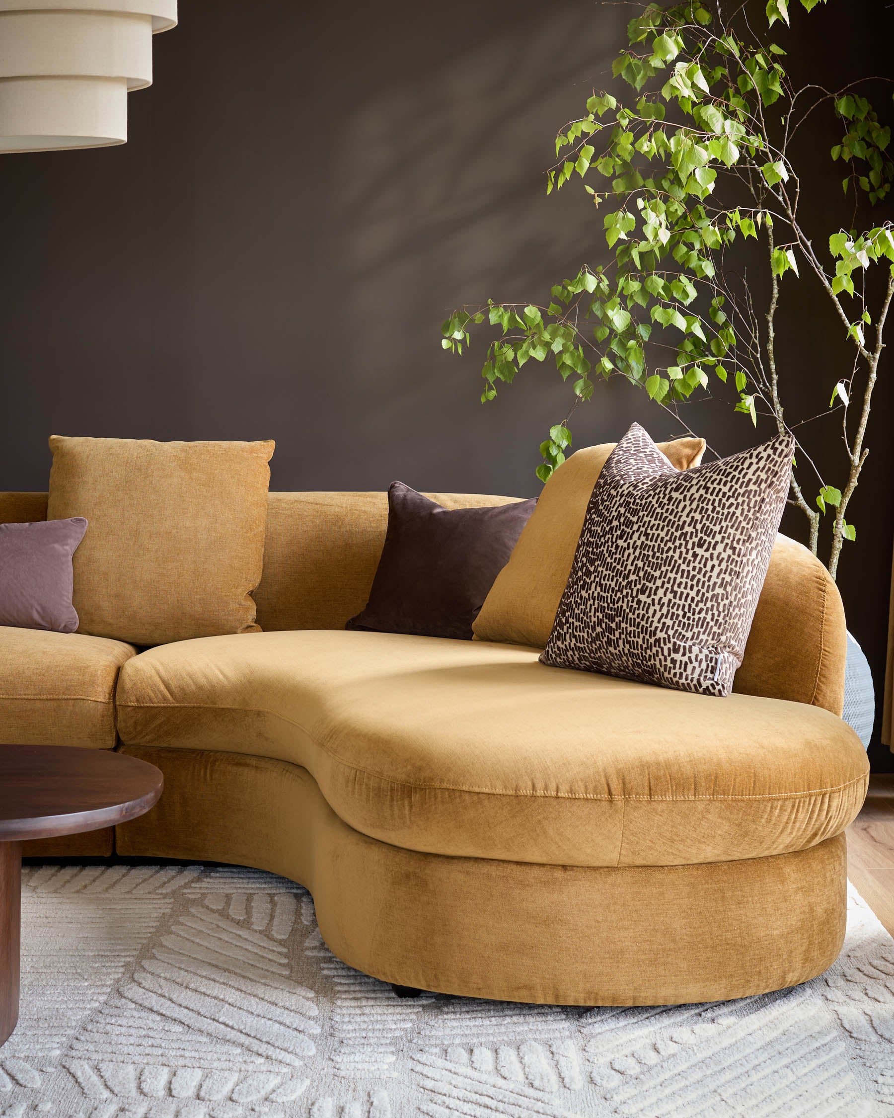 Ochre fabric right-hand corner chaise sofa with curved design and decorative pillows in a styled living room setting.