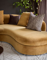 Ochre right-hand corner chaise sofa with curved design, styled with patterned and solid cushions against dark wall.