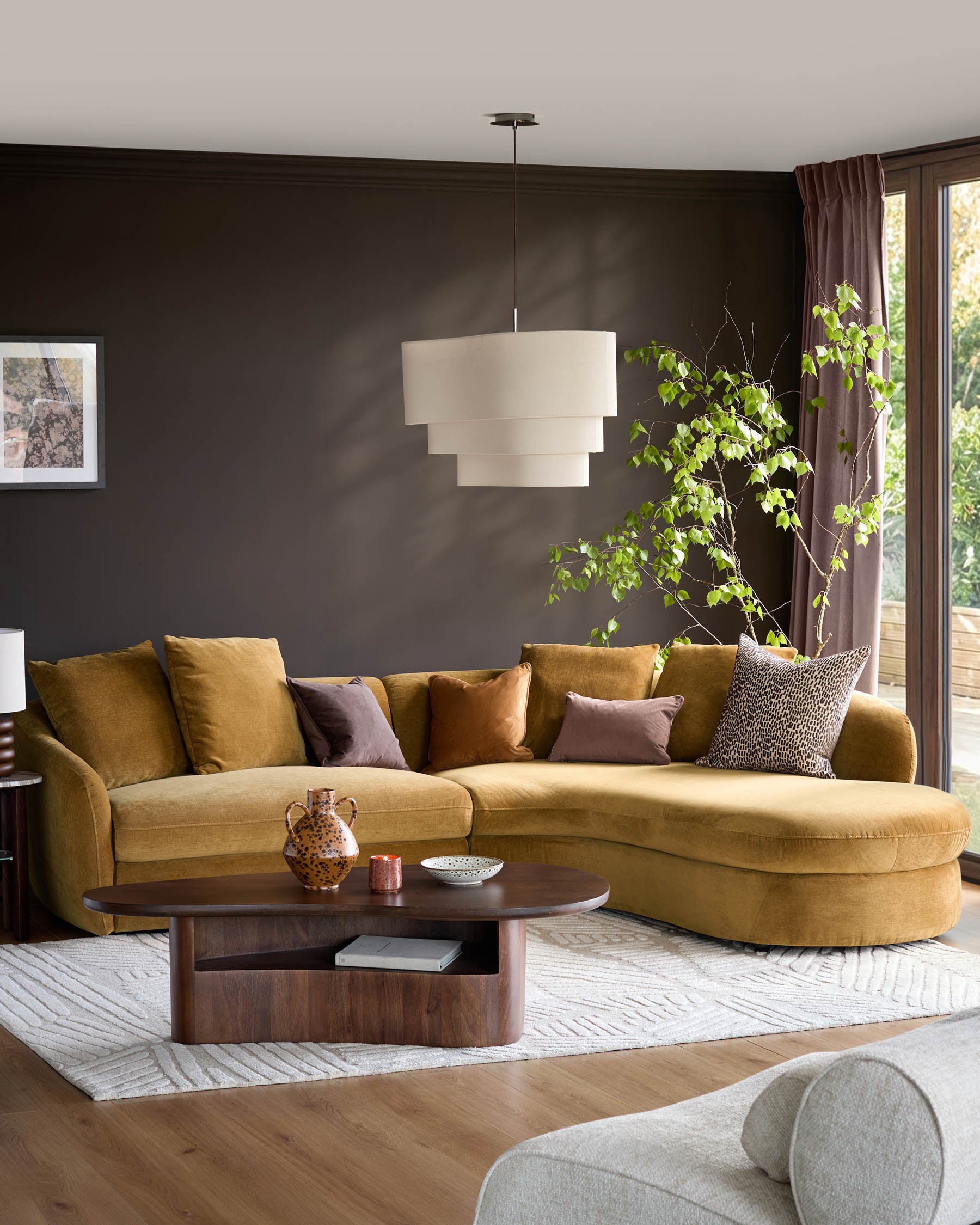 Ochre right-hand corner chaise sofa with curved design, shown in a modern living room setting with dark walls and styled with accent pillows.