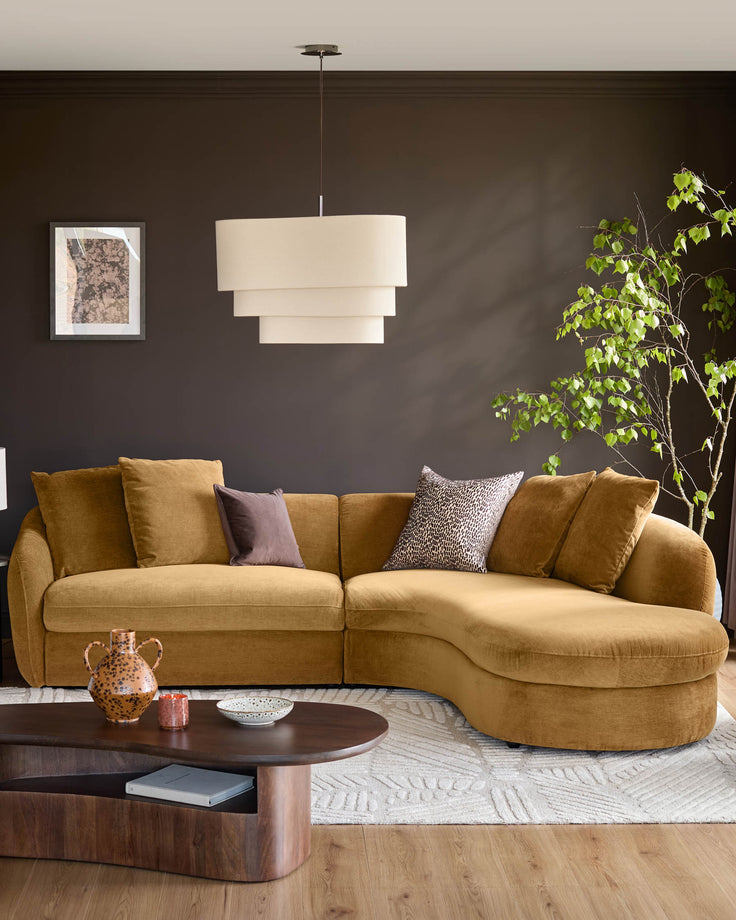 Ochre fabric right-hand corner chaise sofa with curved design and decorative cushions in a dark modern living room.