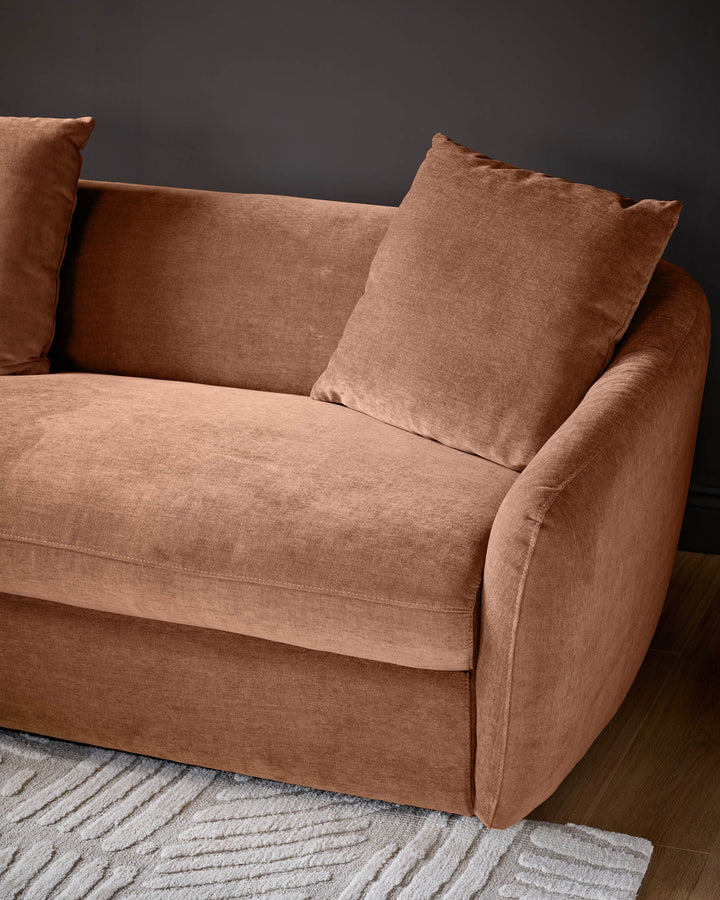 Apricot fabric left-hand corner chaise sofa with rounded arms and decorative pillows, angled view on striped rug.