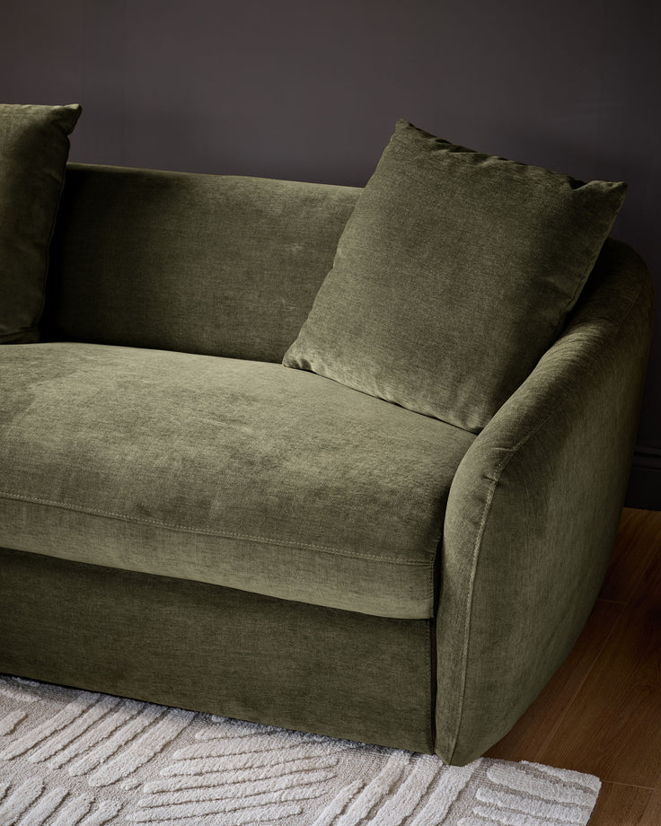Olive green left-hand corner chaise sofa with rolled arms and matching cushions on striped rug.