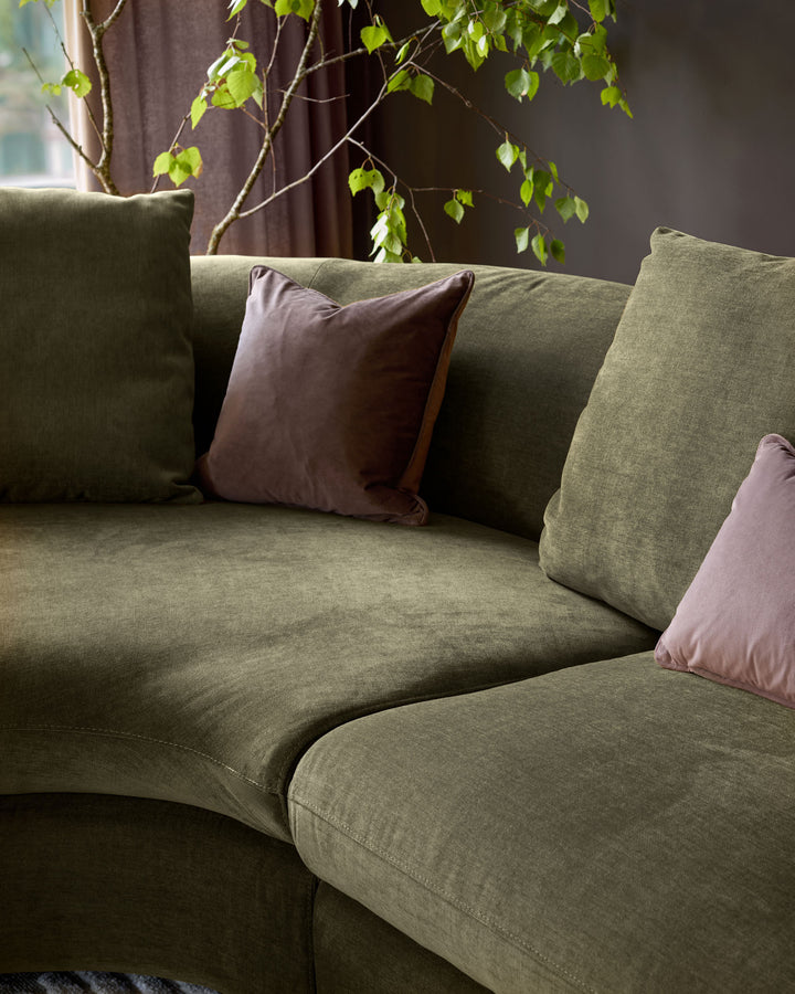 Olive green left-hand corner chaise sofa with mauve and brown scatter cushions, styled with trailing ivy plant.