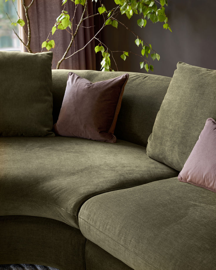 Olive green left-hand corner chaise sofa with mauve and brown scatter cushions, styled with trailing ivy plant.