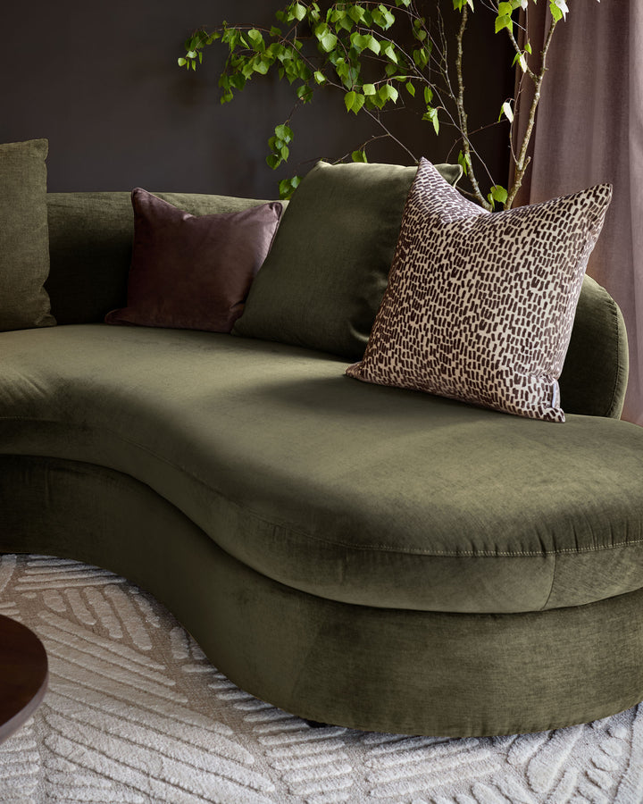 Ottilie right-hand corner chaise sofa in olive green fabric, styled with decorative pillows and a potted plant against a dark wall.
