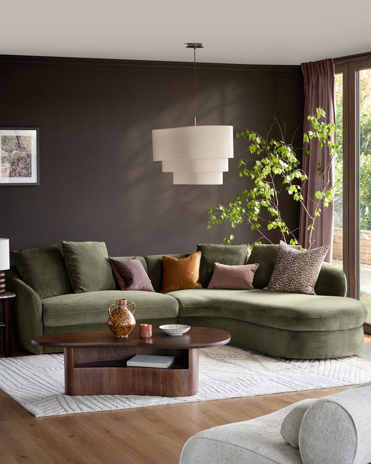 Olive-green corner chaise sofa with right-hand chaise, displayed in a dark-walled living room with decorative pillows and wooden coffee table.