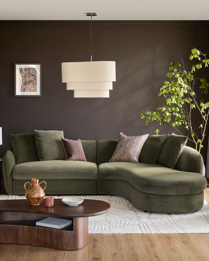 Olive-green corner chaise sofa with curved right-hand chaise, styled in a modern living room with dark walls and decorative pillows.