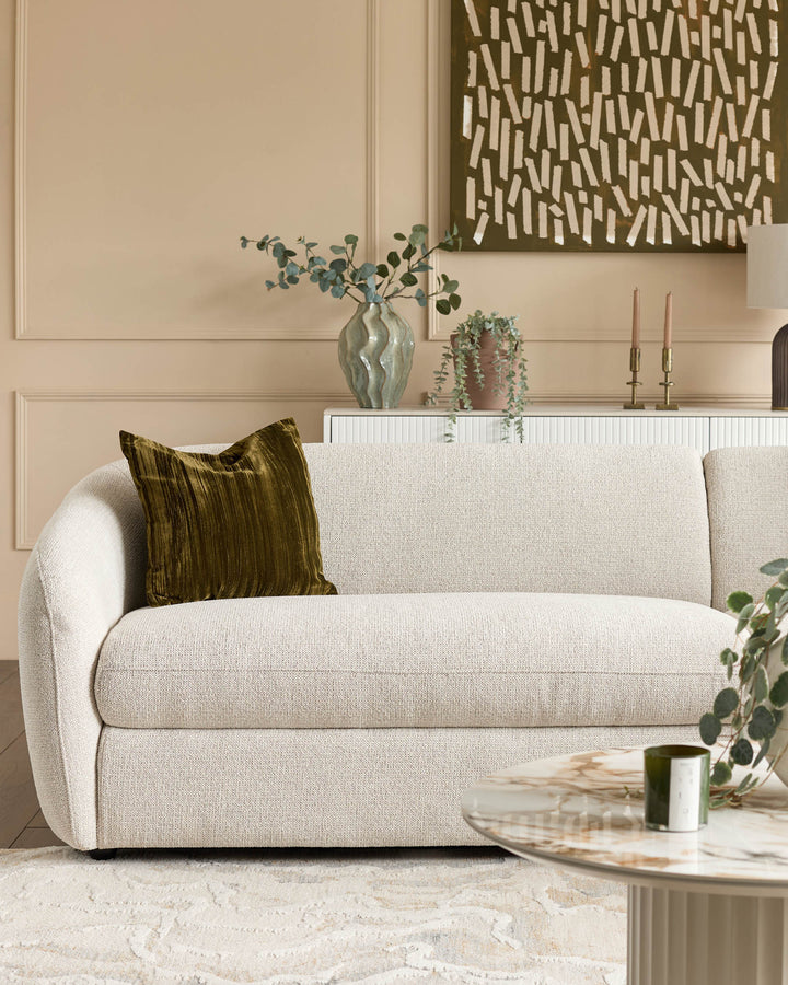 Cream curved sofa with rounded arms and a green striped pillow, styled in a modern living room setting.