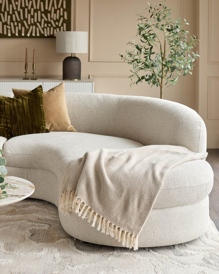 Cream curved chaise sofa with rounded arms, styled with gold and olive pillows and a cream throw blanket in a modern living room.