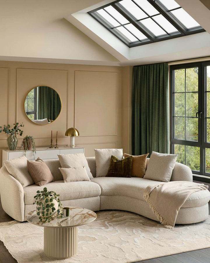 Ottilie right-hand corner chaise sofa in natural fabric, curved design with rounded arms and multiple scatter cushions in a bright living room setting.