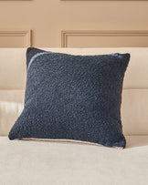 Navy textured cushion with cream trim displayed on a beige upholstered sofa against paneled wall backdrop.