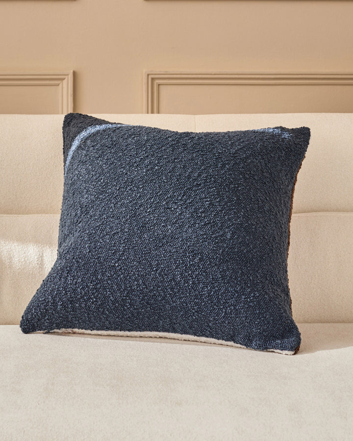 Navy textured cushion with cream trim displayed on a beige upholstered sofa against paneled wall backdrop.
