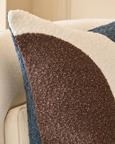 Harmony cushion in navy with cream and brown color-blocking, displayed on a cream chair showing textured fabric detail.