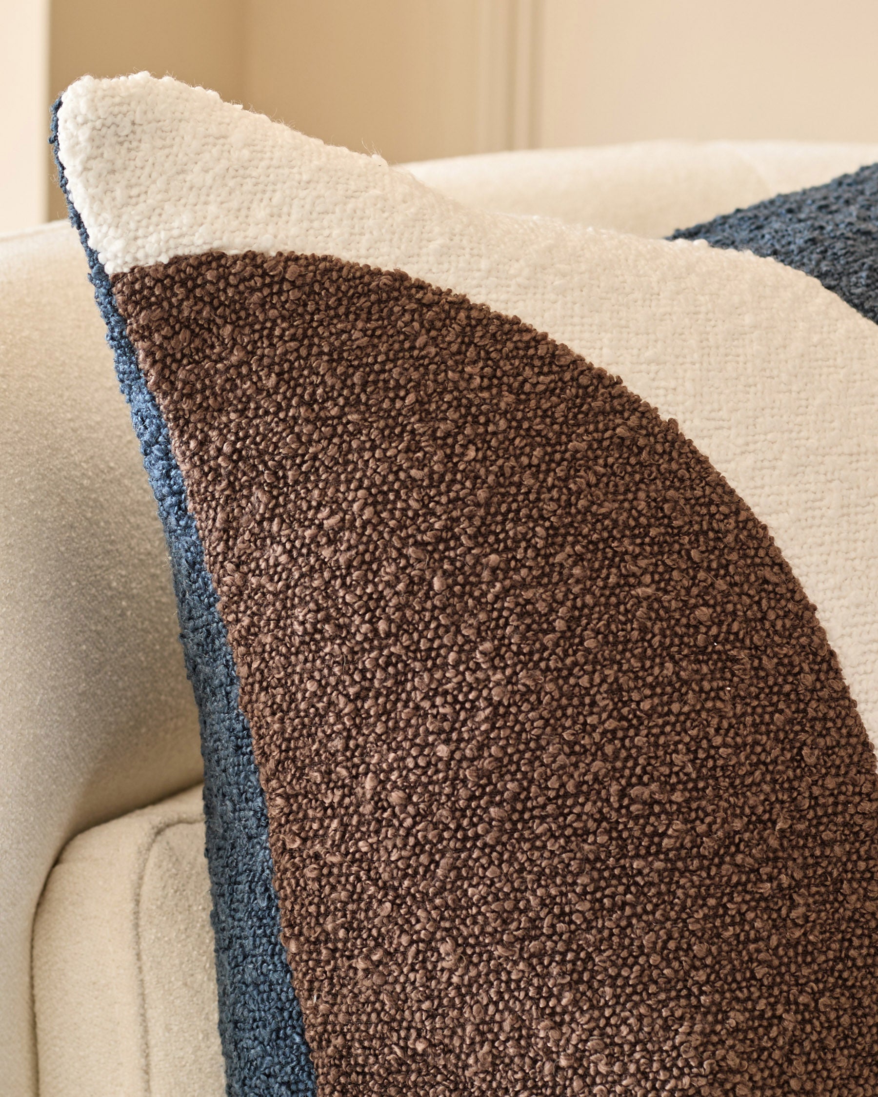Harmony cushion in navy with cream and brown color-blocking, displayed on a cream chair showing textured fabric detail.