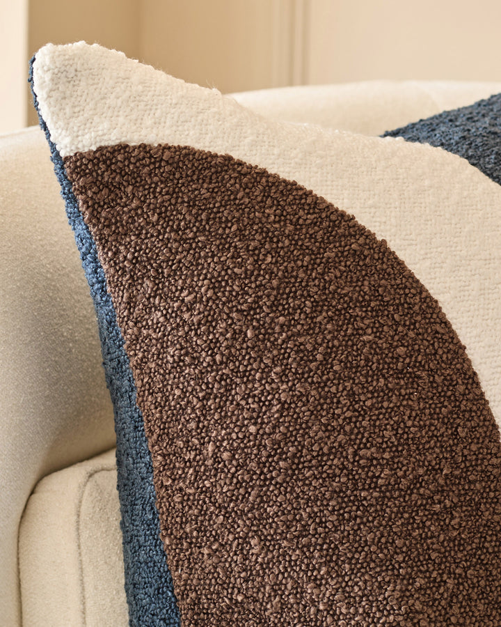 Harmony cushion in navy with cream and brown color-blocking, displayed on a cream chair showing textured fabric detail.