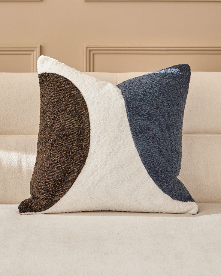 Harmony Cushion in navy, medium size, displayed on a beige sofa showing its abstract curved design in brown, cream, and navy.