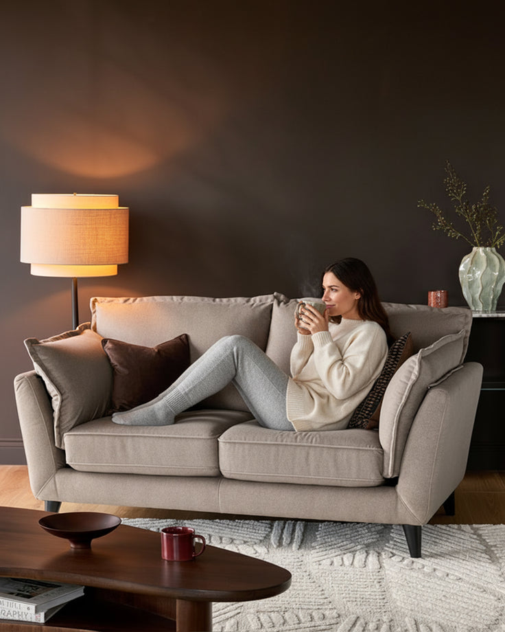 Otto 2-seater sofa in mocha fabric, displayed in a living room setting with a woman seated on it holding a mug.