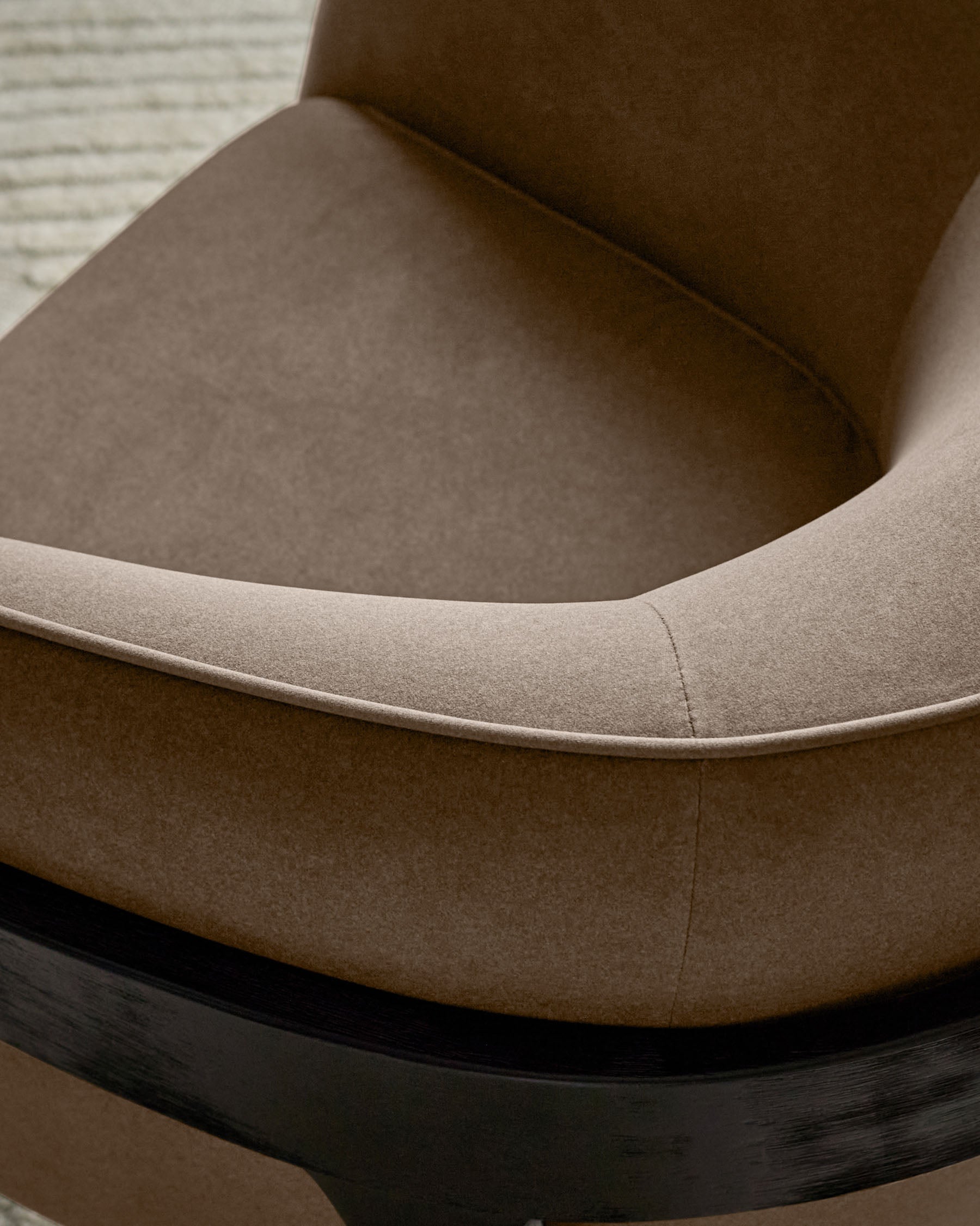 Palmer occasional chair in mocha fabric, close-up detail of curved armrest and black wooden base.