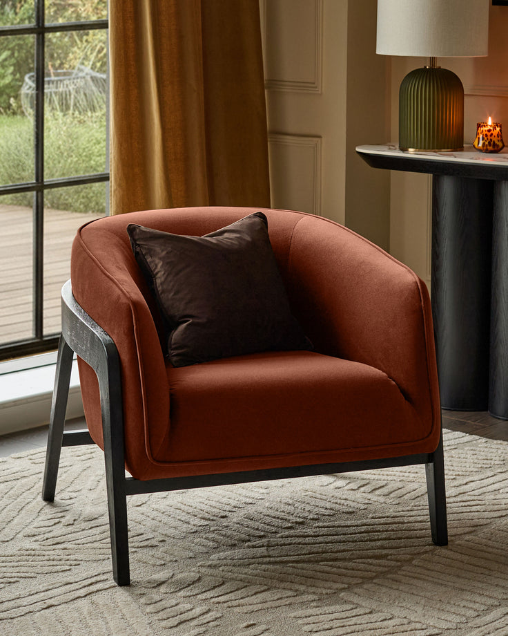 Palmer occasional chair in toffee-red fabric with dark wooden frame and black leather accent pillow, shown in styled interior setting.