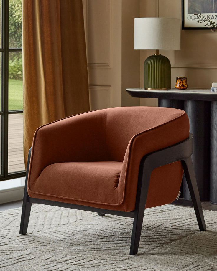 Palmer Occasional Chair in toffee-red fabric with black wooden legs, shown in a styled living room setting.
