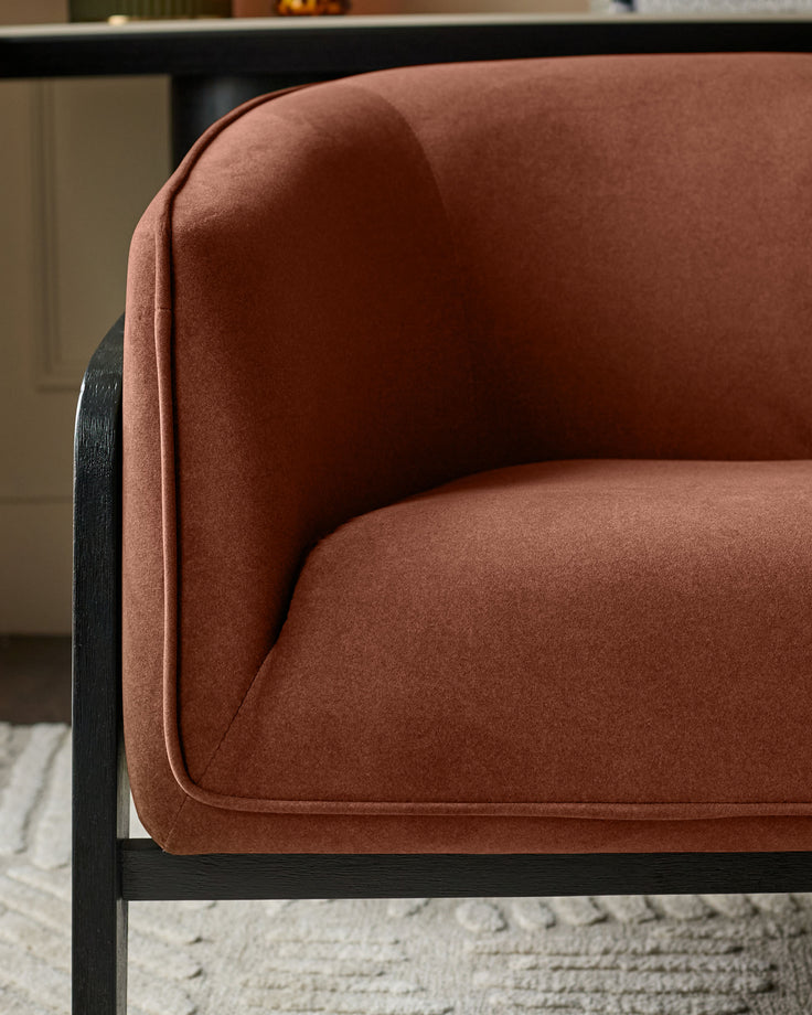 Palmer Occasional Chair in toffee-red fabric with curved backrest and black wooden frame, side view detail.