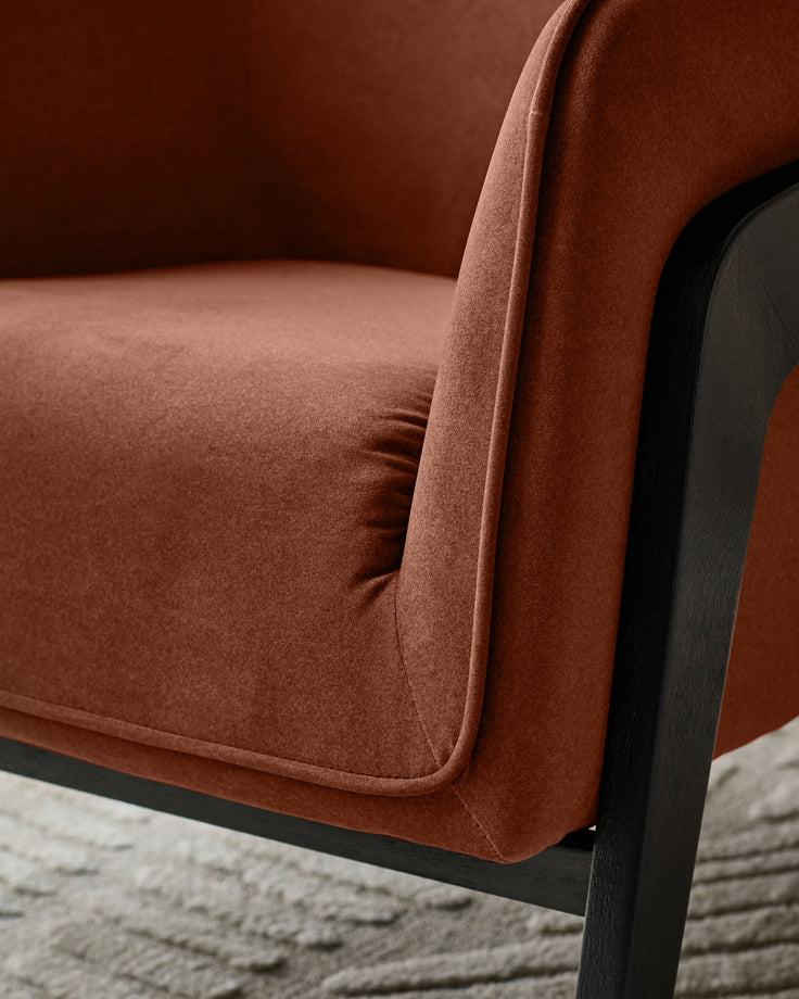 Palmer occasional chair in toffee-red fabric with black wooden frame, shown from side angle on Grey rug.
