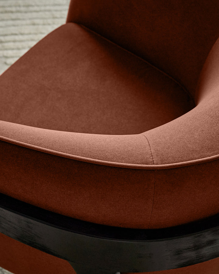 Palmer Occasional Chair in toffee-red fabric, close-up detail showing curved armrest and black wooden base.