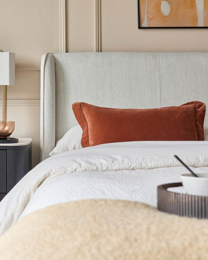 Bedroom featuring a fabric headboard, bedside table with lamp, neutral wall panelling, and a breakfast tray on the bed.