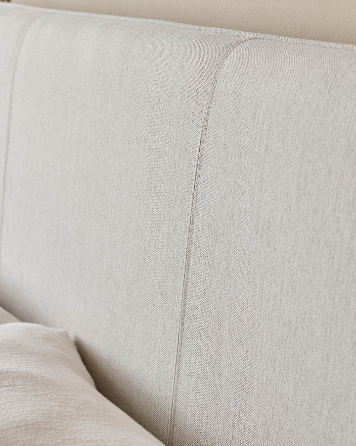 Close-up of a beige fabric headboard with a padded design and a cushion in the foreground.