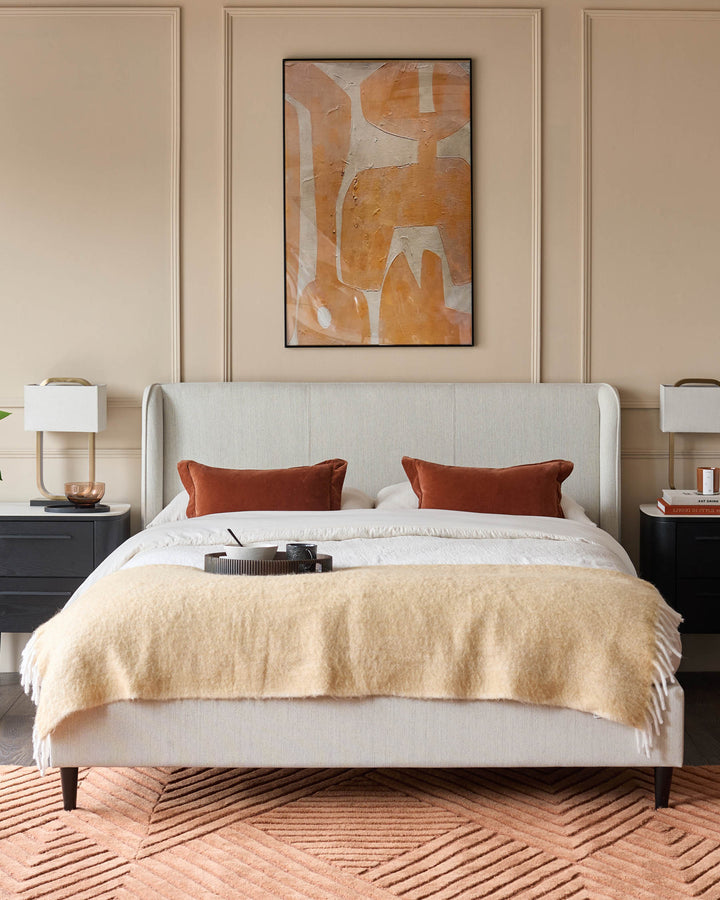 A neutral bedroom showcases a linen headboard bed flanked by dark bedside tables and a stylish rug.