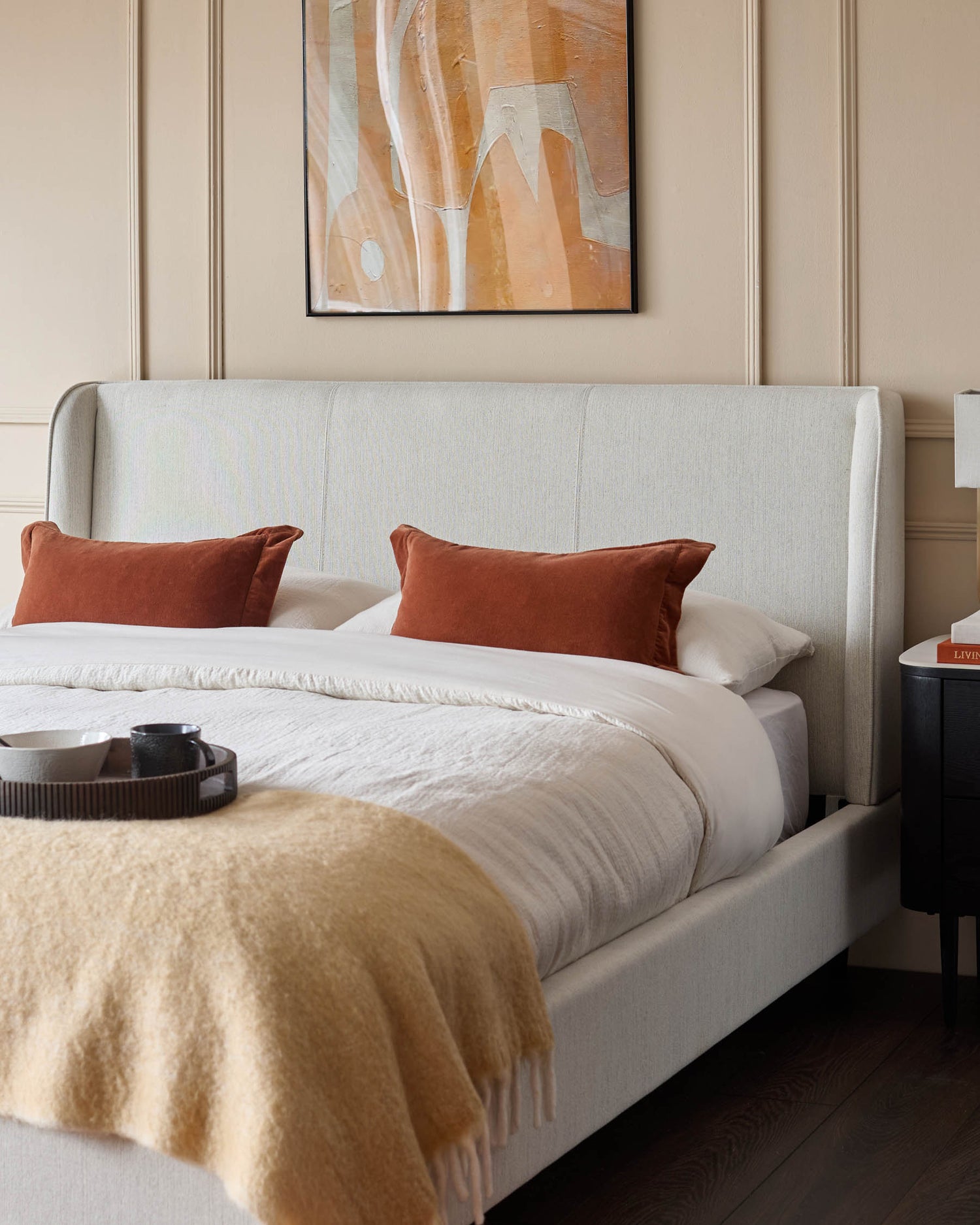 Bedroom furniture featuring a bed with neutral-toned linen headboard, side table, bedding, and a framed print.