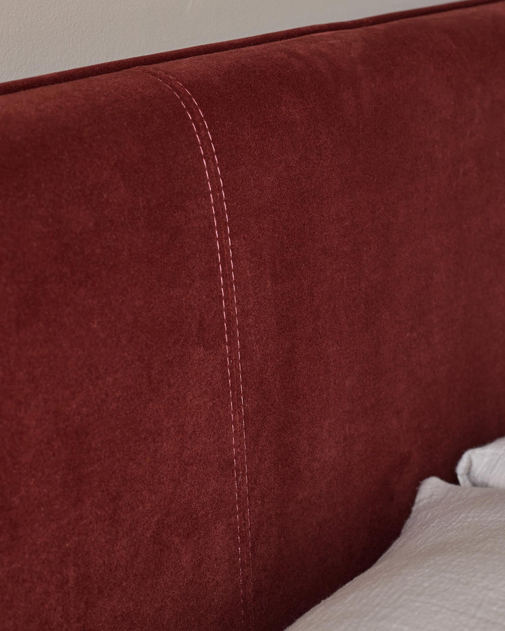Close-up of a headboard with vertical stitched detailing and soft red fabric.