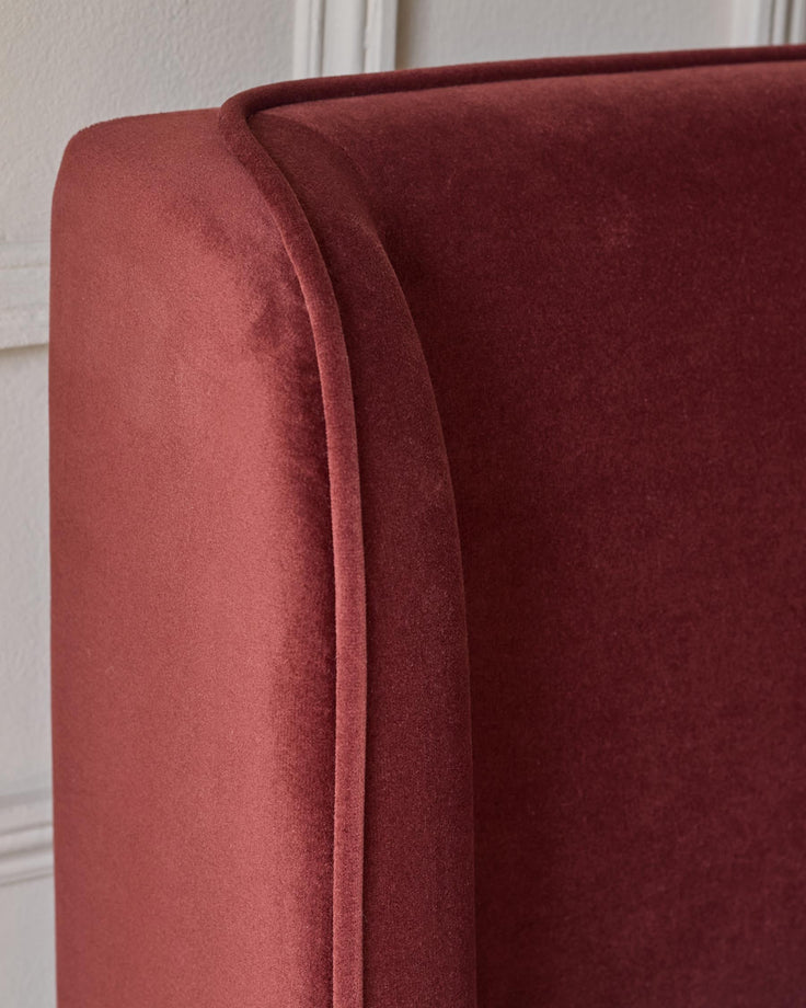 Close-up of a burgundy velvet headboard with a subtle seam detail. A classic and elegant addition to any bedroom.