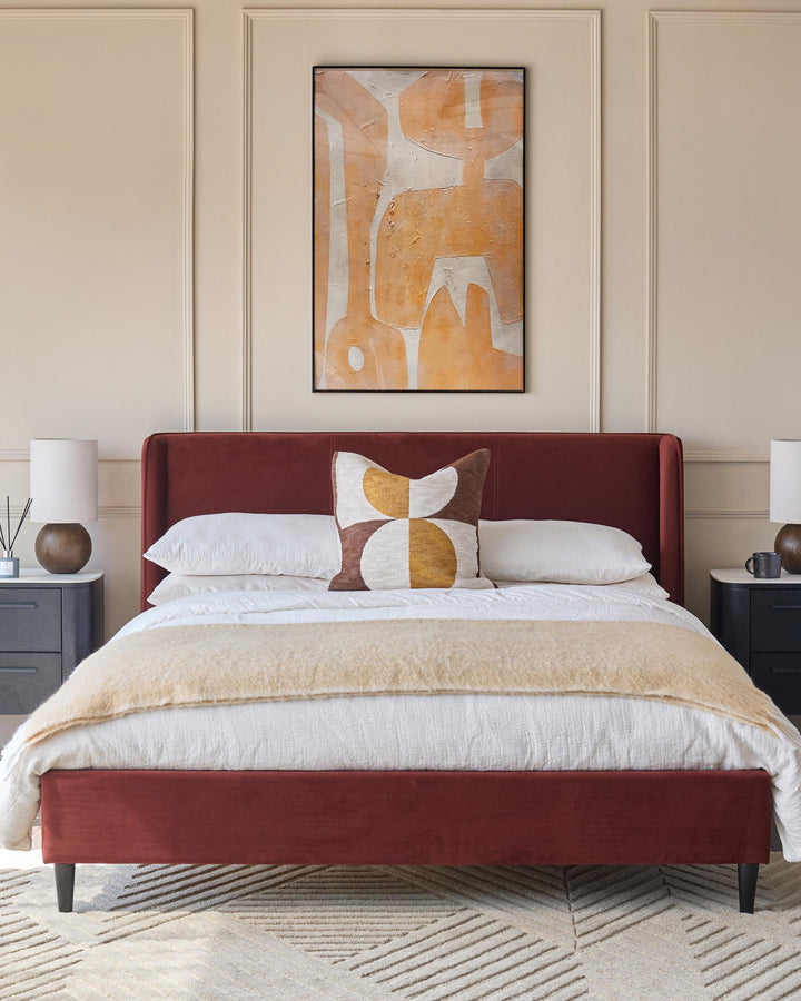 A stylish bedroom featuring a plush red bed, framed artwork, and complementary bedside tables and lamps.