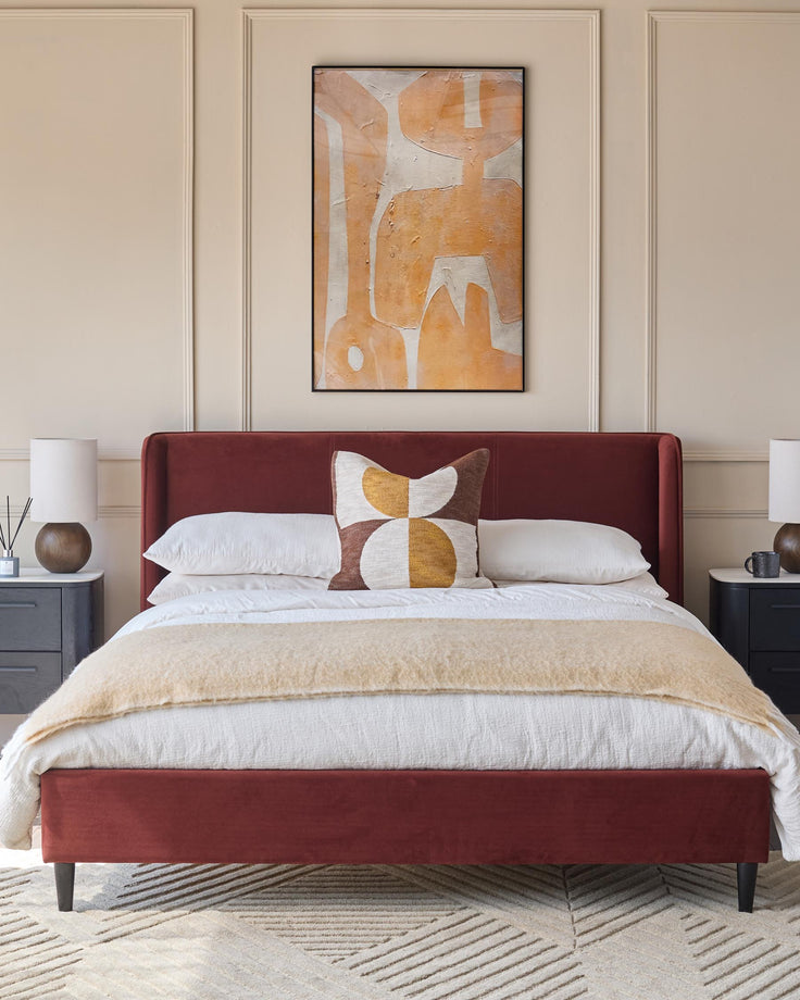 A stylish bedroom featuring a plush red bed, framed artwork, and complementary bedside tables and lamps.