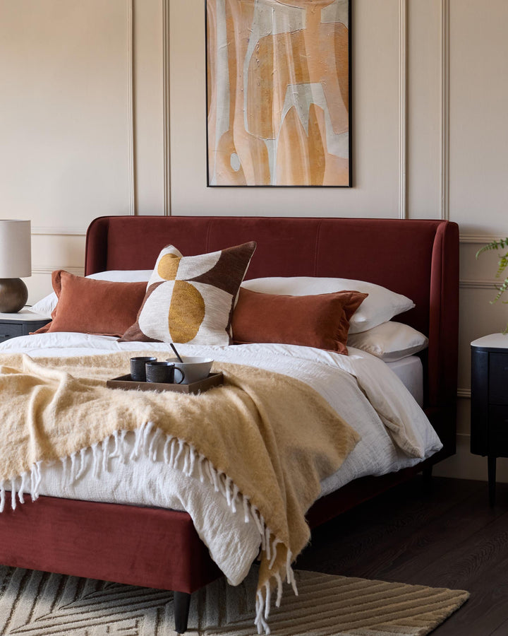 Stylish bedroom featuring a red upholstered bed, bedside tables, abstract art and soft, textured throws and cushions.
