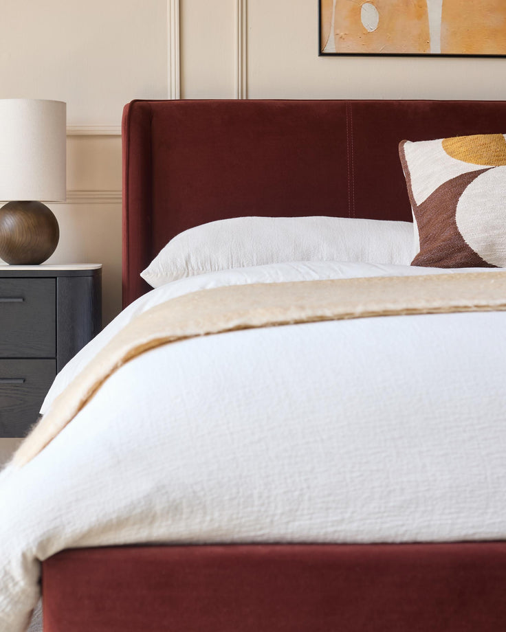A stylish bedroom setup, featuring a bed with a striking red headboard, paired with a chic bedside table and lamp.