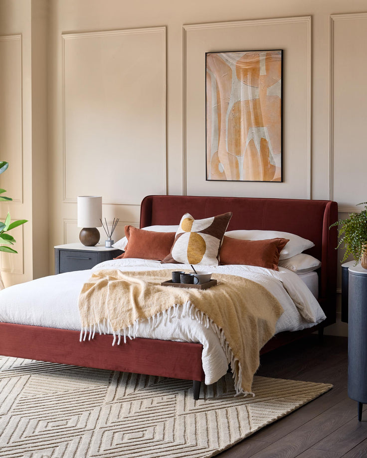 A contemporary bedroom featuring a red velvet bed, stylish side tables, and a geometric rug.