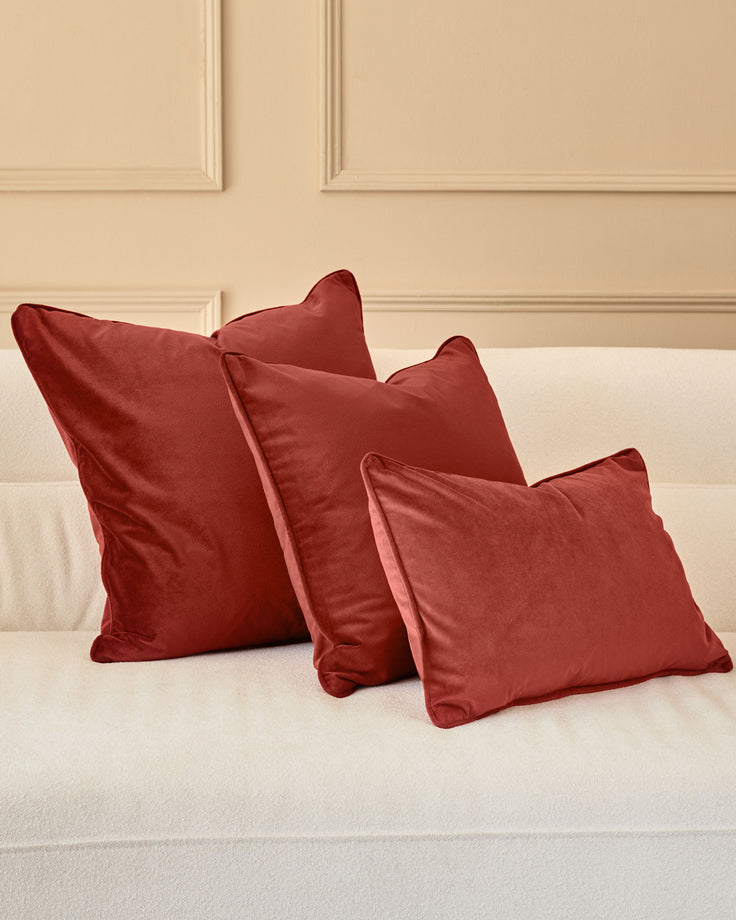 Three burgundy rectangular cushions arranged on a cream bed against a beige paneled headboard.