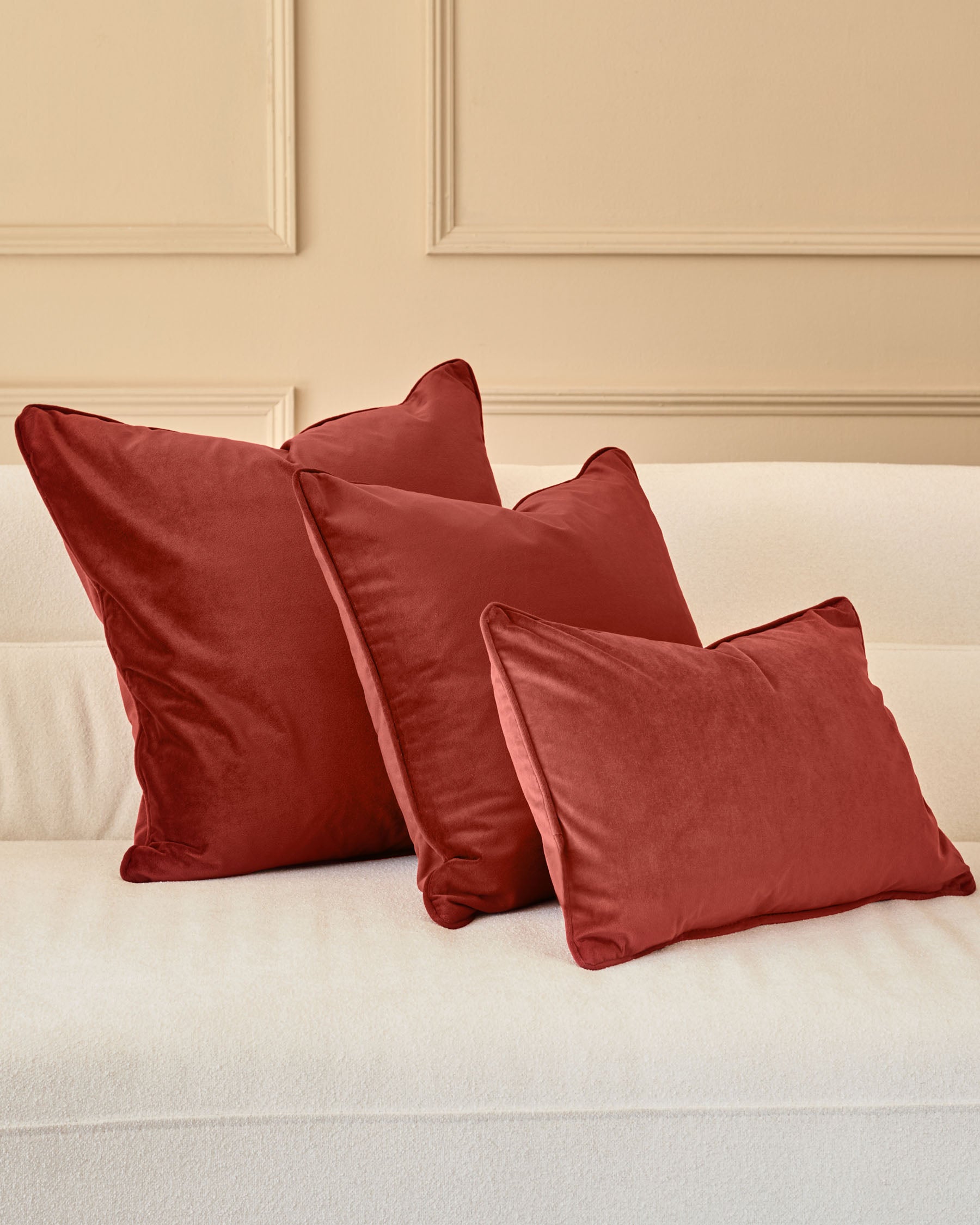 Large toffee red cushion displayed on a cream bed with coordinating pillows, showing plump fill and soft fabric texture.